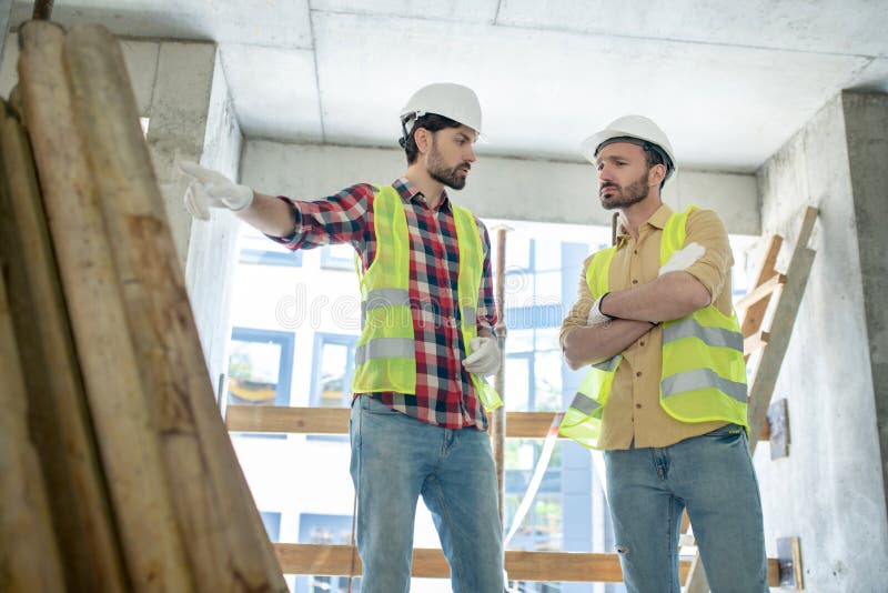 Building workers in yellow vests and gloves standing near pile of boards, discussing what to do with them stock images