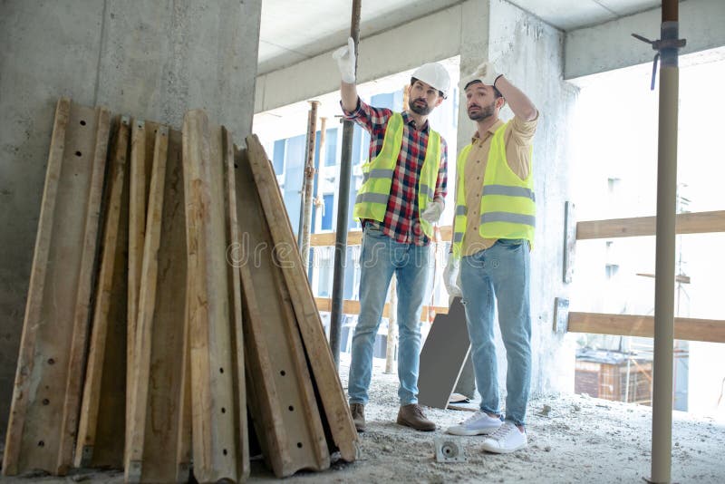 Building workers in yellow vests and gloves standing near pile of boards, discussing what to do with them royalty free stock image