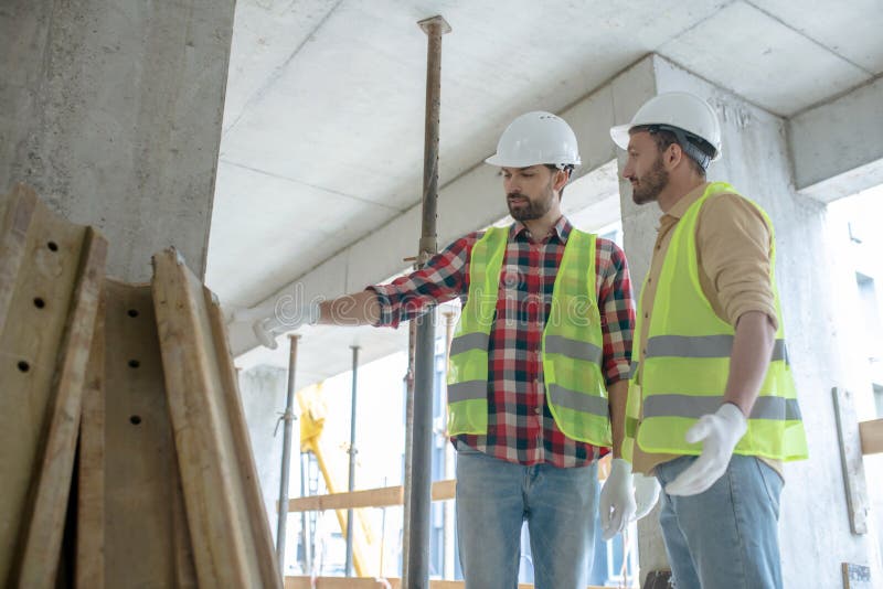 Building workers in yellow vests and gloves standing near pile of boards, pointing at them stock photos