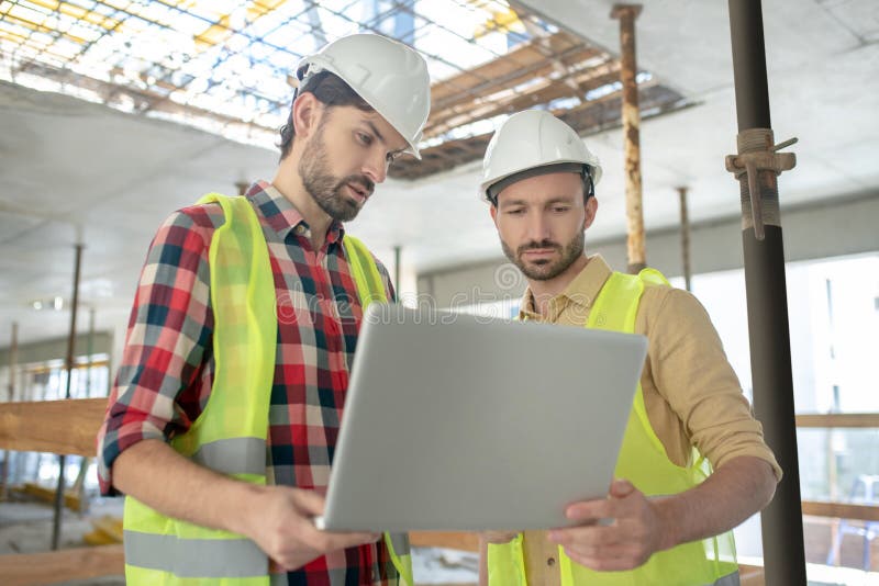 Building workers in yellow vests holding laptop, checking something on it royalty free stock photos