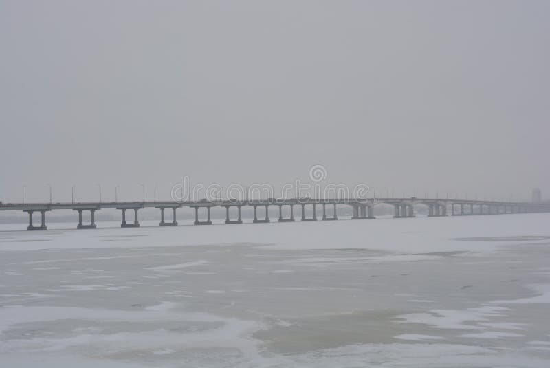 Very cold weather, the landscape of a new winter bridge across the Dnipro river to the left side of the city with ice on the river.