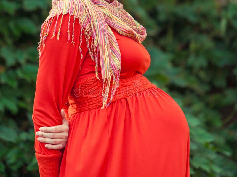 Buk av en gravid kvinna i en röd klänning royaltyfri bild Buk av en gravid kvinna i en röd klänning royaltyfri bild