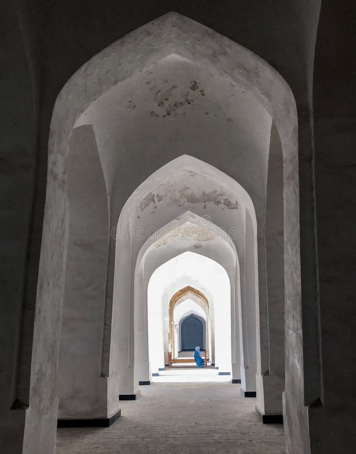 Bukhara, Uzbekistan, April 2018: Kalyan Mosque. A corridor of white arches, through which you can see a bench with a Muslim woman