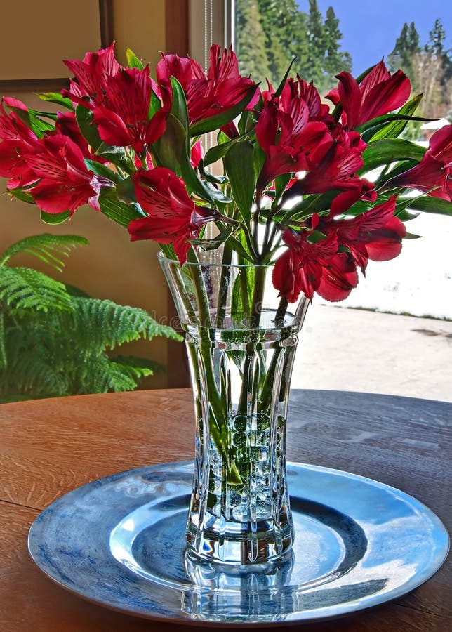 This vertical stock image is a bouquet of red lily flowers in a crystal vase of vase. Outside the glass door is a snowy winter day. This vertical stock image is a bouquet of red lily flowers in a crystal vase of vase. Outside the glass door is a snowy winter day.