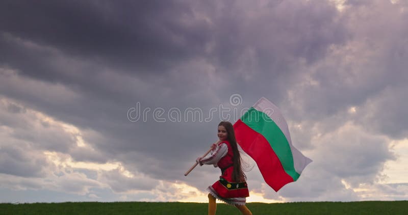 Bulgaars meisje standaard drager van etnisch folklore kostuum met bulgaarse vlag op groen veld bulgarije