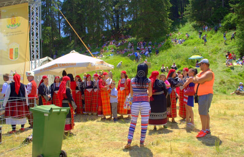 Women folklore singers group dressed in traditional authentic bright red Rodopian costumes at Folklore Festival Rozhen in beautiful scenery of Rhodope Mountains.Every 4th year in July, Bulgarians of all over the country gather below the peak of Rozhen for a festival, where singers and instrumentalists sing and play on a several scenes. Women folklore singers group dressed in traditional authentic bright red Rodopian costumes at Folklore Festival Rozhen in beautiful scenery of Rhodope Mountains.Every 4th year in July, Bulgarians of all over the country gather below the peak of Rozhen for a festival, where singers and instrumentalists sing and play on a several scenes.