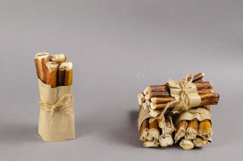 Bully sticks for dogs wrapped in brown paper and tied with twine. Portioned grouped Beef pizzle for pets. Popular Chewing treats on gray background. Air-dried stock photos