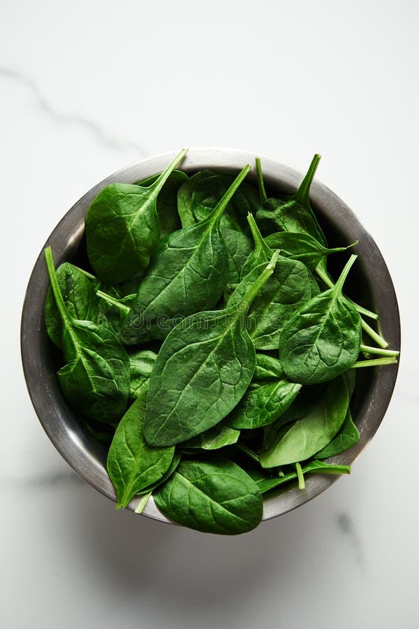 A bunch of Fresh baby spinach leaves in the in a stainless steel bowl on white marble background. stock photography A bunch of Fresh baby spinach leaves in the in a stainless steel bowl on white marble background. stock photography