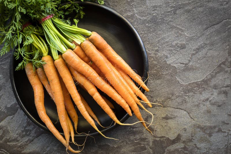 Bunch of Raw Baby Carrots in Rustic Black Bowl Over Slate Stock Photo