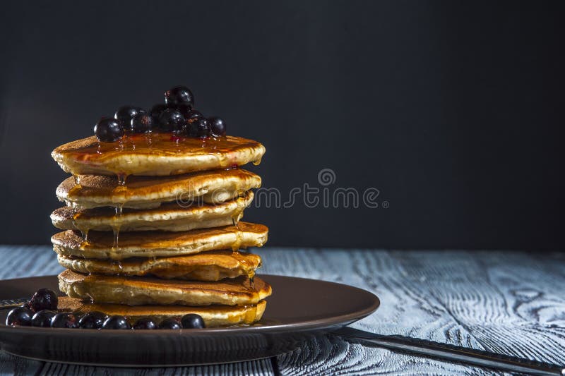 Bunt av hemlagade pannkakor med bär och honung på den bruna plattan på lantlig bakgrund arkivfoton Bunt av hemlagade pannkakor med bär och honung på den bruna plattan på lantlig bakgrund arkivfoton