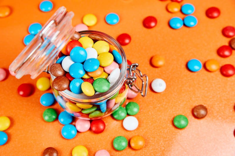 Bunte Süßigkeiten im Glasgefäß auf rotem Orangenhintergrund stockbild Bunte Süßigkeiten im Glasgefäß auf rotem Orangenhintergrund stockbild