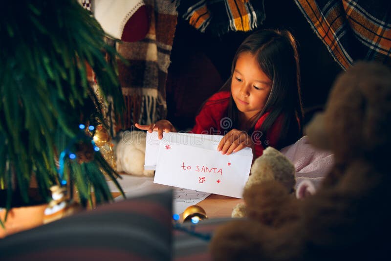 Buon Natale e feste felici La ragazza sveglia del piccolo bambino scrive la lettera a Santa Claus vicino all'albero di Natale fotografia stock libera da diritti Buon Natale e feste felici La ragazza sveglia del piccolo bambino scrive la lettera a Santa Claus vicino all'albero di Natale fotografia stock libera da diritti