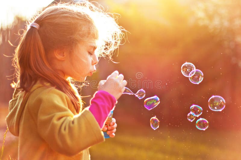 Burbujas de jabón de la muchacha del niño que soplan al aire libre