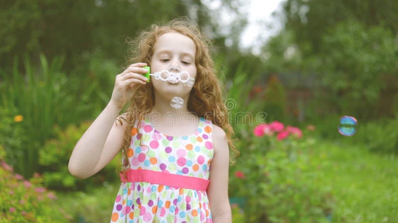 Burbujas de jabón de la muchacha que soplan cabelluda rizada feliz en parque del verano metrajes