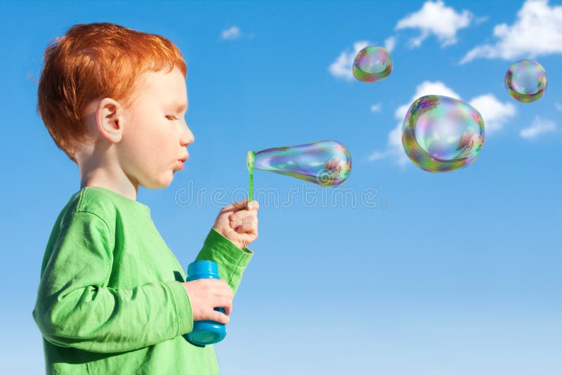 Burbujas de jabón del niño del muchacho que soplan en el cielo