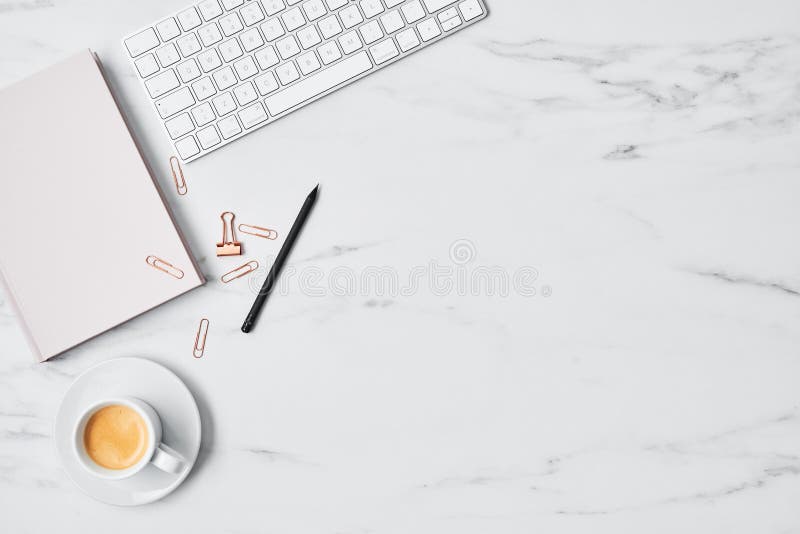 Office desk with computer, coffee cup, pink diary and paper clips on white marble background. Flat lay. Copy space for text. Top view. Office desk with computer, coffee cup, pink diary and paper clips on white marble background. Flat lay. Copy space for text. Top view