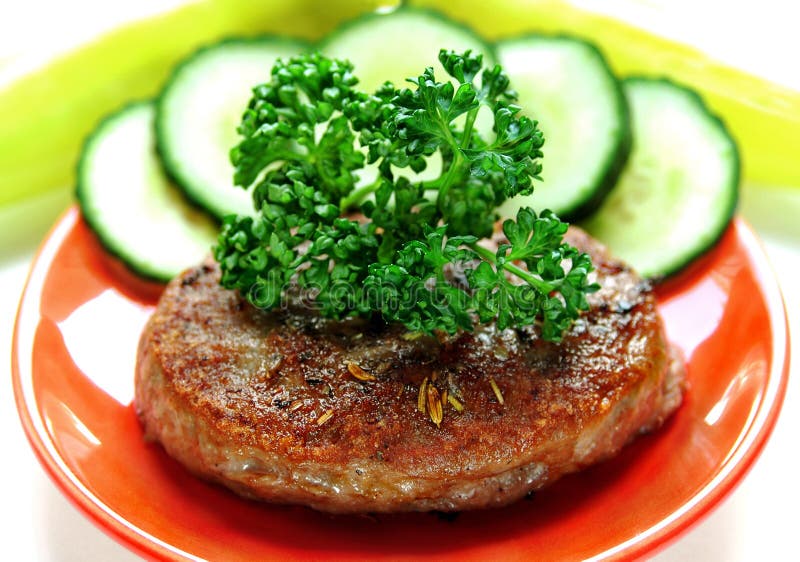 Hamburger decorato cetriolo, verde peperoni un prezzemolo sul piatto, isolato su sfondo bianco,.