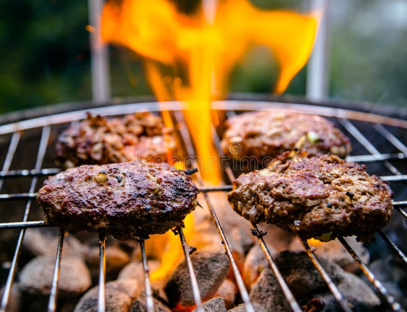 Hamburgers cooking on an outside grill with flaming charcoal briquettes. Hamburgers cooking on an outside grill with flaming charcoal briquettes.