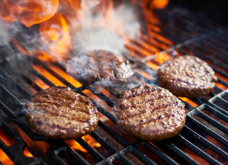 Burgers μαγειρέματος στην καυτή σχάρα με τις φλόγες στοκ εικόνες