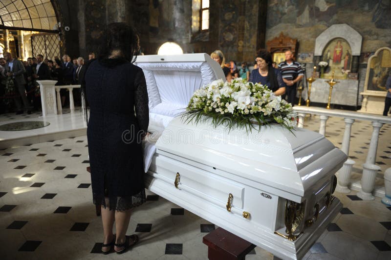 Burial service in a church: woman dressed in black mourning clothes standing in front of the white coffin with late