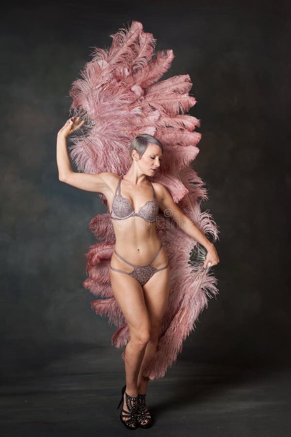 A burlesque dancer poses demurely with pink feather fans behind her body. A burlesque dancer poses demurely with pink feather fans behind her body.