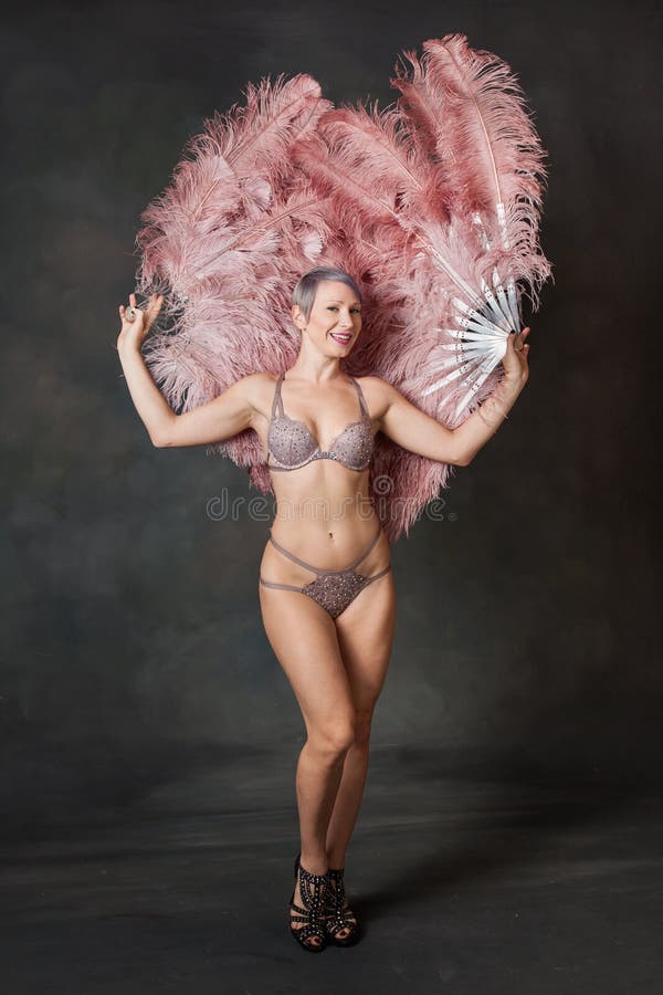 A burlesque dancer walks forward with feather fans behind her. A burlesque dancer walks forward with feather fans behind her.