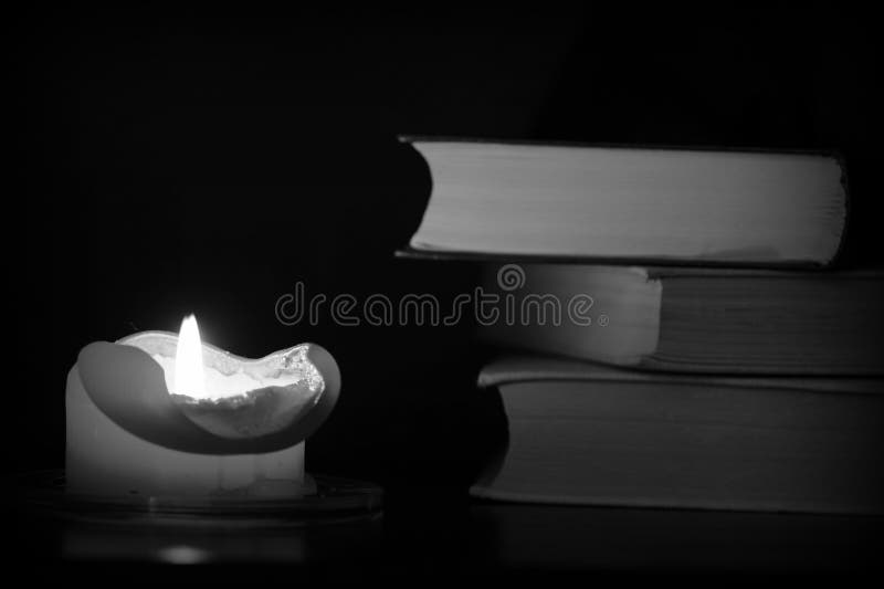 Burning Candle and Old Books in the Dark. Black and White Stock Photo