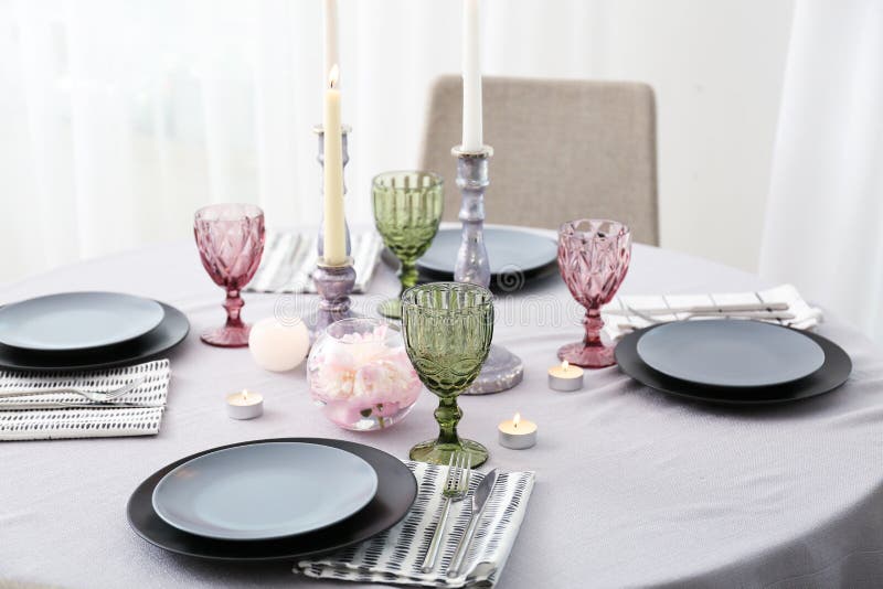 Burning candles with dishware and cutlery on table in dining room