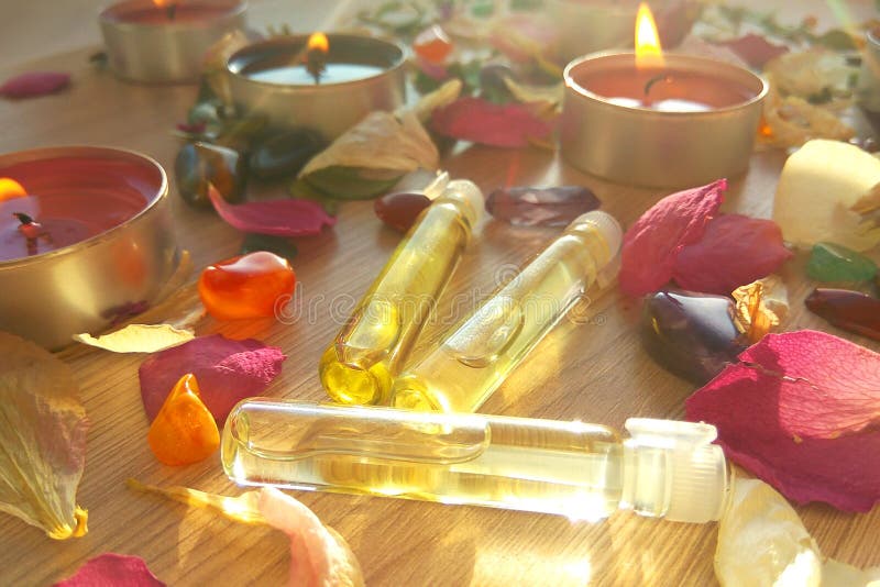 Burning candles with essential spa oil, rose flower petals and colorful gems on wooden background stock images