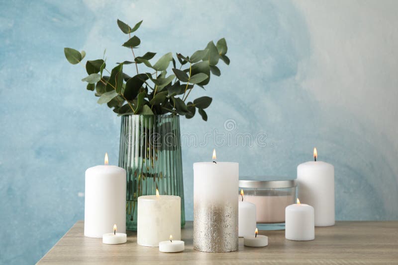 Burning candles and vase with eucalyptus on table against blue background, space for text stock image