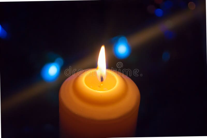 A burning orange candle on a dark background with blue lights - a Christmas New Year`s eve divination mystic esoteric royalty free stock photo A burning orange candle on a dark background with blue lights - a Christmas New Year`s eve divination mystic esoteric royalty free stock photo