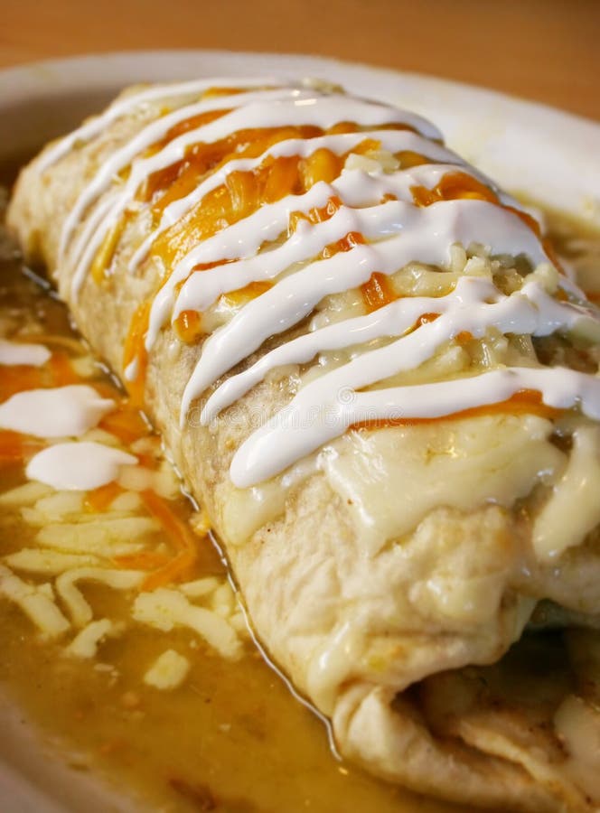 Stuffed burrito lies on a plate in the restaurant covered with sour cream and green sauce ready to be eaten