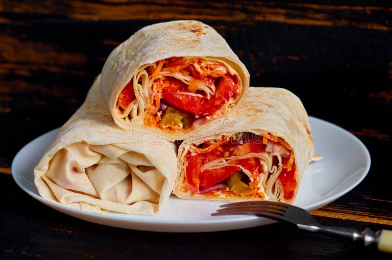 Burrito vegetariano con las verduras frescas en la placa blanca adornada con la bifurcación de plata en fondo de madera negro de foto de archivo libre de regalías Burrito vegetariano con las verduras frescas en la placa blanca adornada con la bifurcación de plata en fondo de madera negro de foto de archivo libre de regalías