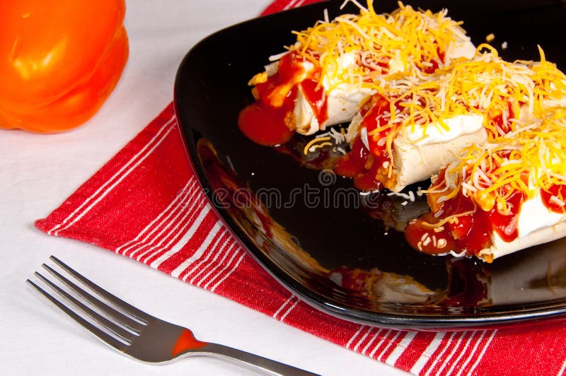 Three Burritos covered in Sour Cream, Enchilada Sauce, and Shredded Cheese on a Black Plate on a Red Cloth. Three Burritos covered in Sour Cream, Enchilada Sauce, and Shredded Cheese on a Black Plate on a Red Cloth.