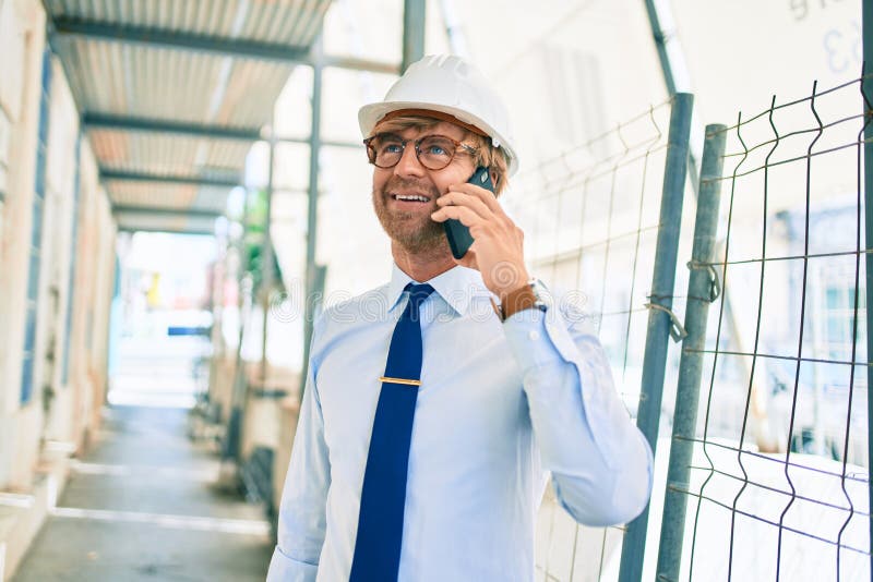 Business architect man wearing hardhat standing outdoors of a building project speaking on the phone stock photo