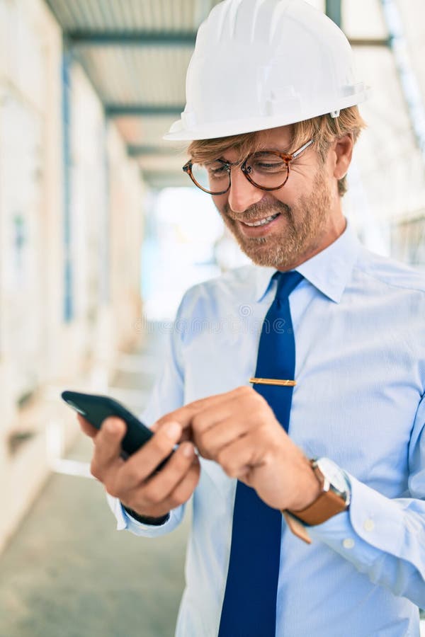 Business architect man wearing hardhat standing outdoors of a building project using smartphone stock images