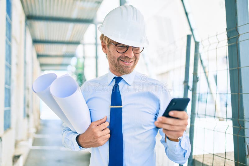 Business architect man wearing hardhat standing outdoors of a building project using smartphone royalty free stock image