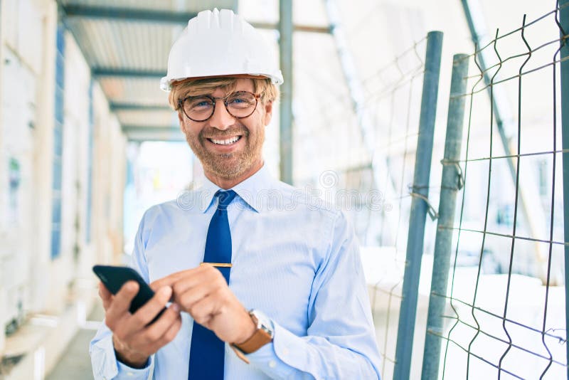 Business architect man wearing hardhat standing outdoors of a building project using smartphone stock photo