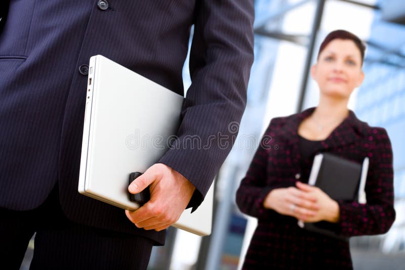 Close-up of hand of businessman holding laptop computer and mobile phone, businesswoman standing behind holding notebook. Male hand holding businessman stock images, royalty-free photos and pictures