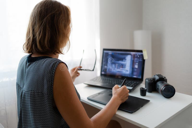 Business and creativity. A young blonde in glasses does retouching, there is a camera on the table. Back view stock photography Business and creativity. A young blonde in glasses does retouching, there is a camera on the table. Back view stock photography