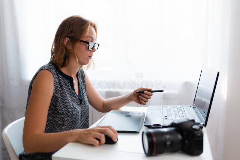 Business and creativity. Young woman in glasses working on a laptop. On the table is a camera and a tablet