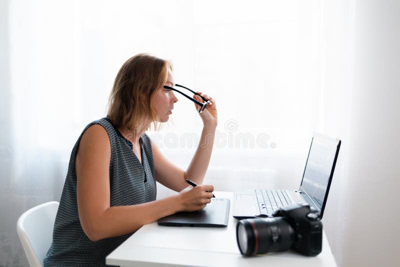 Business and creativity. A young woman wears glasses doing retouching, on the table is a camera