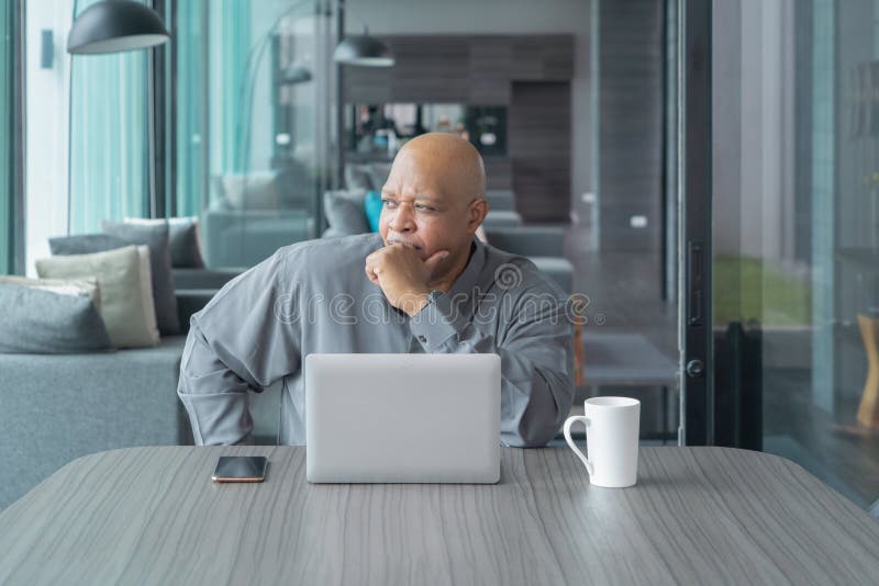 Business elderly black american man, African person working from home, thinking about problem with computer notebook laptop and