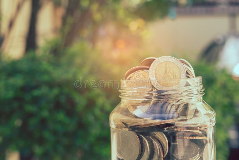 Business and Financial Concept : Close up money coins in savings money glass jar with green bush in the background. stock photography Business and Financial Concept : Close up money coins in savings money glass jar with green bush in the background. stock photography