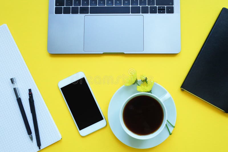 Business flat lay: desk with notebook, pencil, cup of coffee on yellow table...