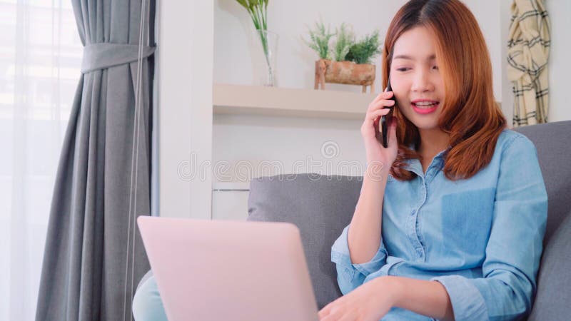 Business freelance Asian woman working on laptop and talking on phone with customer while sitting on table in living room. stock photos Business freelance Asian woman working on laptop and talking on phone with customer while sitting on table in living room. stock photos