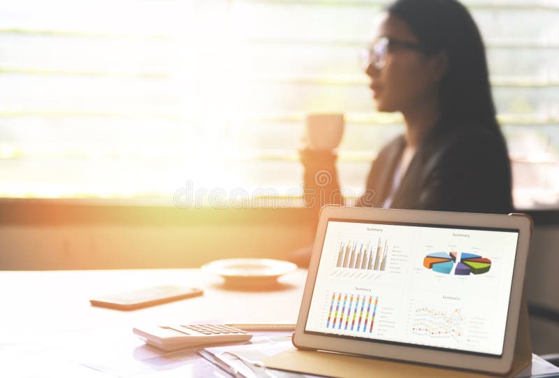 Business graphs chart on a tablet computer technology on the table and woman working in office with coffee cup - Sale report money