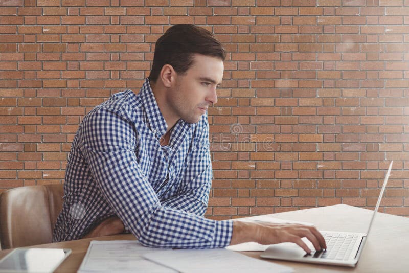 Digital composite of Business man at a desk using a computer against brick wall