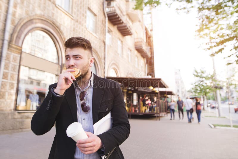 Business man with documents in his hands eats a snack while walking to work stock images