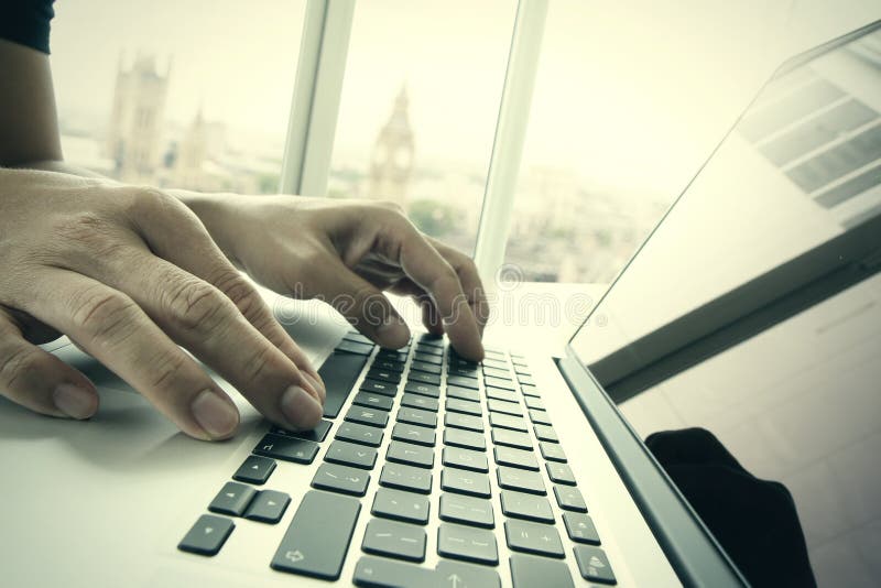 Business man hand working on laptop computer on wooden desk with london city blurred background as concept